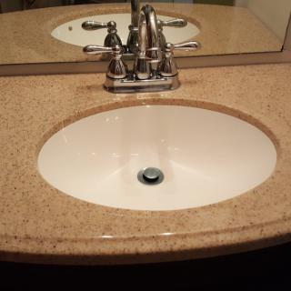 A bathroom sink with a faucet set in a granite countertop, reflected in a mirror.