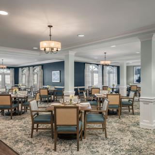 A spacious and elegant dining room with multiple tables and chairs, featuring chandeliers and large windows.