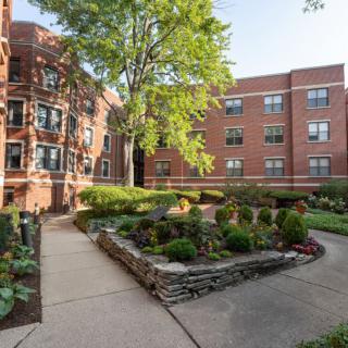 A serene courtyard surrounded by brick apartment buildings, featuring a well-maintained garden and pathway.