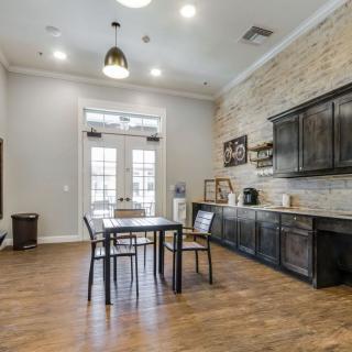 A modern kitchen and dining area featuring a wooden table, chairs, and dark cabinets against a brick accent wall.