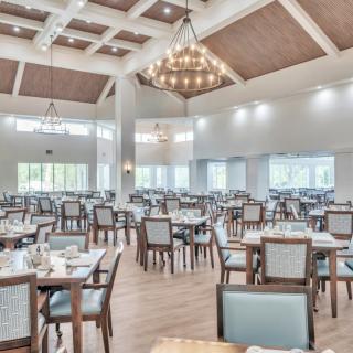 A spacious dining hall with neatly arranged tables and chairs, illuminated by elegant chandeliers.
