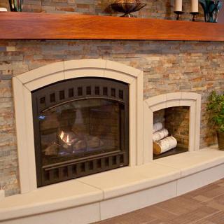 A cozy indoor fireplace with a stone wall, adorned with decor items and neatly stacked logs beside it.