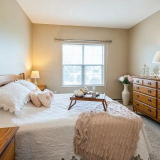 A cozy bedroom with soft lighting and warm decor elements, showcasing a neatly made bed, wooden furniture, and a window letting in natural light.