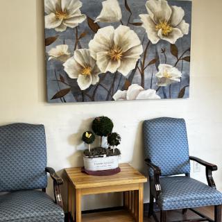 A cozy waiting area featuring elegant floral artwork, comfortable chairs, and a small decorative plant.