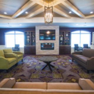 A spacious living room with a high ceiling, elegant chandelier, and comfortable seating arranged around a central table.