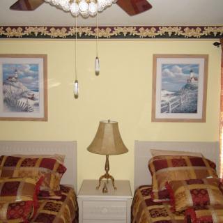 A cozy bedroom featuring twin beds, a lamp on a nightstand, and decorative paintings on the wall.