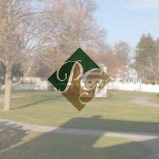 A decorative stained glass design visible through a window, showcasing a blend of green and gold with an outdoor landscape in the background.