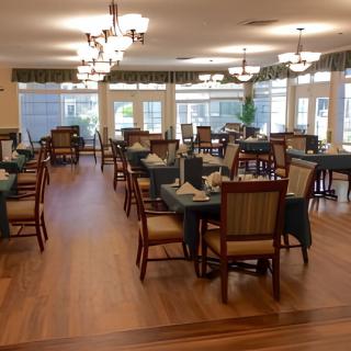 A spacious dining area featuring neatly arranged tables and chairs with elegant chandeliers and ample natural light.