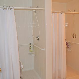 A bathroom with two shower stalls featuring white curtains.