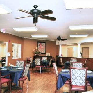 A well-lit dining room with set tables and chairs, featuring ceiling fans and warm decor.