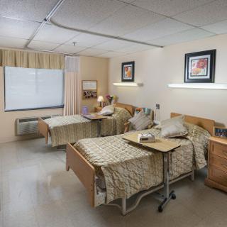 A spacious hospital patient room featuring two beds, bedside tables, and ample natural light.