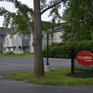A hotel with a parking lot and sign in a green, outdoor setting.