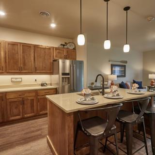 A modern kitchen with wooden cabinets and an island, featuring pendant lighting and stainless steel appliances.