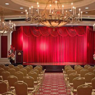 A grand theater with red curtains and rows of seating, illuminated by elegant chandeliers.