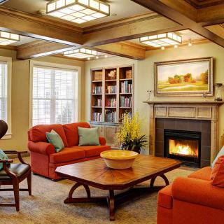 A cozy living room featuring vibrant orange sofas, a wooden coffee table, and a warm fireplace, with bookshelves and decorative artwork enhancing the inviting atmosphere.