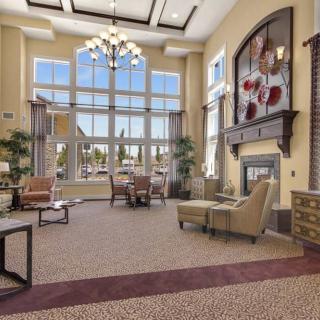 A spacious and cozy living room with a large chandelier, comfortable seating, and a fireplace, enhanced by natural light from big windows.