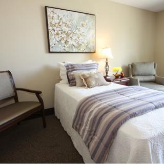 A cozy bedroom with a neatly made bed, decorative pillows, and a wall painting above it.