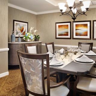 An elegantly decorated dining room with a formal table setting, featuring framed artwork and a central chandelier.