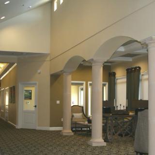 The image shows a spacious lobby with archways and columns, featuring carpet flooring and elegant furniture.
