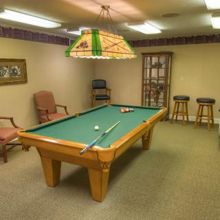 A cozy game room featuring a pool table with cues and chairs arranged around it.