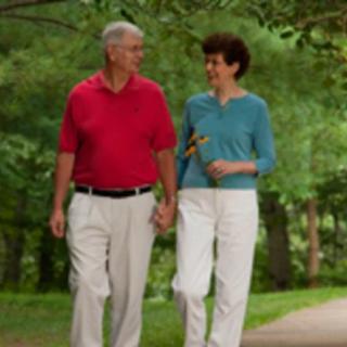 An elderly couple walking hand in hand through a park.