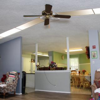 A cozy living room with an open view into the kitchen, featuring a ceiling fan and comfortable seating.