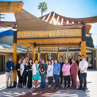 A diverse group of staff members gathered outdoors under a culturally-inspired structure, showcasing unity and community spirit.