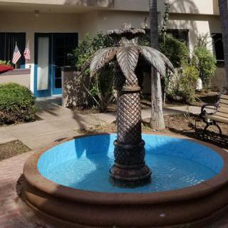 A decorative fountain with a palm tree sculpture stands in a sunny courtyard.