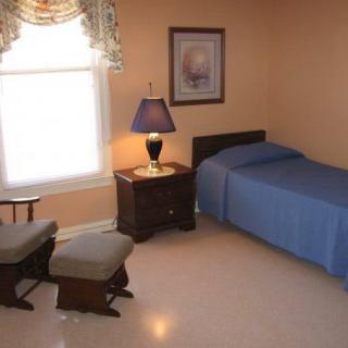 A simple bedroom with a single bed, nightstand, and a rocking chair near the window.