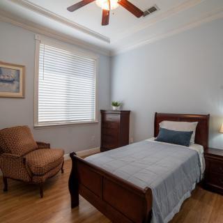 A cozy bedroom with a single bed, armchair, dresser, and a window with blinds.