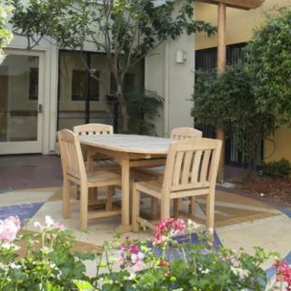 A cozy outdoor garden setting with wooden patio furniture surrounded by greenery and flowers.