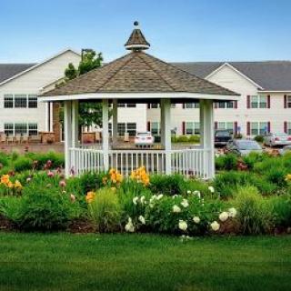 A charming gazebo surrounded by a blooming garden with a large building in the background.