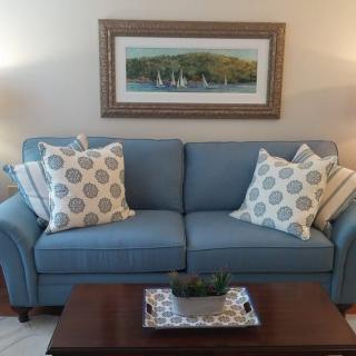 A cozy living room with a blue sofa adorned with patterned throw pillows, complemented by a wooden coffee table and landscape artwork on the wall.