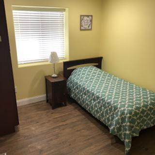 A cozy bedroom featuring a single bed with green bedding and cheerful yellow walls.