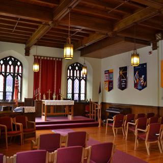 The interior of a chapel featuring an altar, wooden ceiling, and decorative banners.