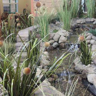 A serene garden scene featuring a tranquil pond surrounded by lush greenery and stones.