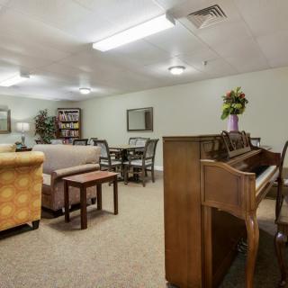 A cozy living room featuring a piano, sofas, tables, and bookshelves.