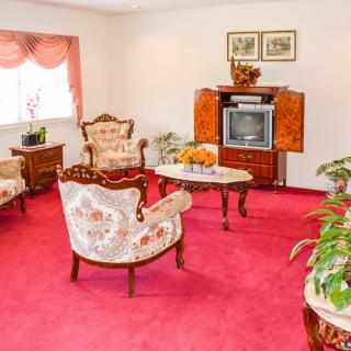 A vintage-style living room with floral upholstered furniture, a red carpet, and a classic television set.