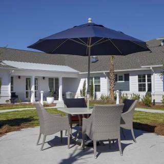 A patio with a table and chairs under a blue umbrella in a backyard setting.