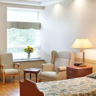 Cozy room with armchairs, a bed, and a table with a lamp and flowers.