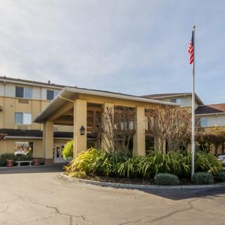 The exterior view of a hotel with an entrance surrounded by well-maintained landscaping and a flagpole.