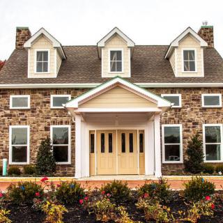 A classic stone facade house with symmetrical windows and a welcoming porch surrounded by landscaped gardens.