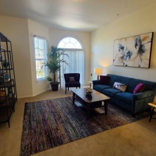 A cozy living room with a blue sofa, coffee table, and decorative elements such as artwork and a large plant near the window.