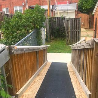 A wooden ramp leading to a grassy area, surrounded by fences and shrubs.