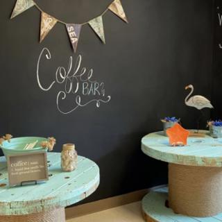 A cozy coffee bar with rustic spool tables and decorative bunting flags against a chalkboard wall.