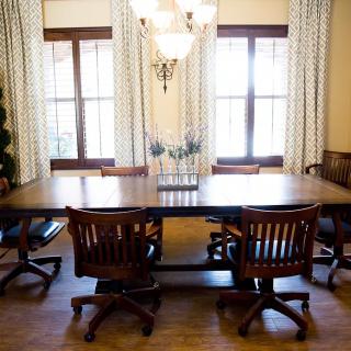 A well-lit meeting room with a large wooden conference table, surrounded by chairs and illuminated by a chandelier.