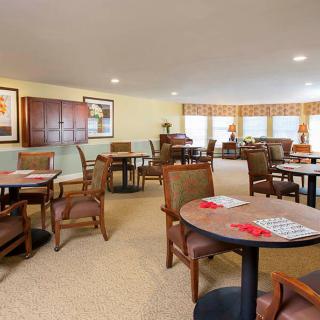 A cozy indoor seating area with multiple tables and chairs, featuring artwork on the walls and ample natural light from large windows.