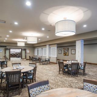 A spacious dining area with round tables, chairs, and modern lighting fixtures.