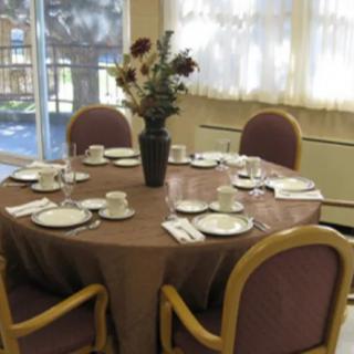 A round dining table is set with plates, cups, and cutlery, adorned with a vase of flowers in the center.