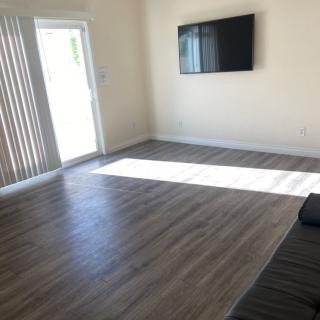 A minimalist living room with natural lighting, featuring a wall-mounted television and hardwood floors.
